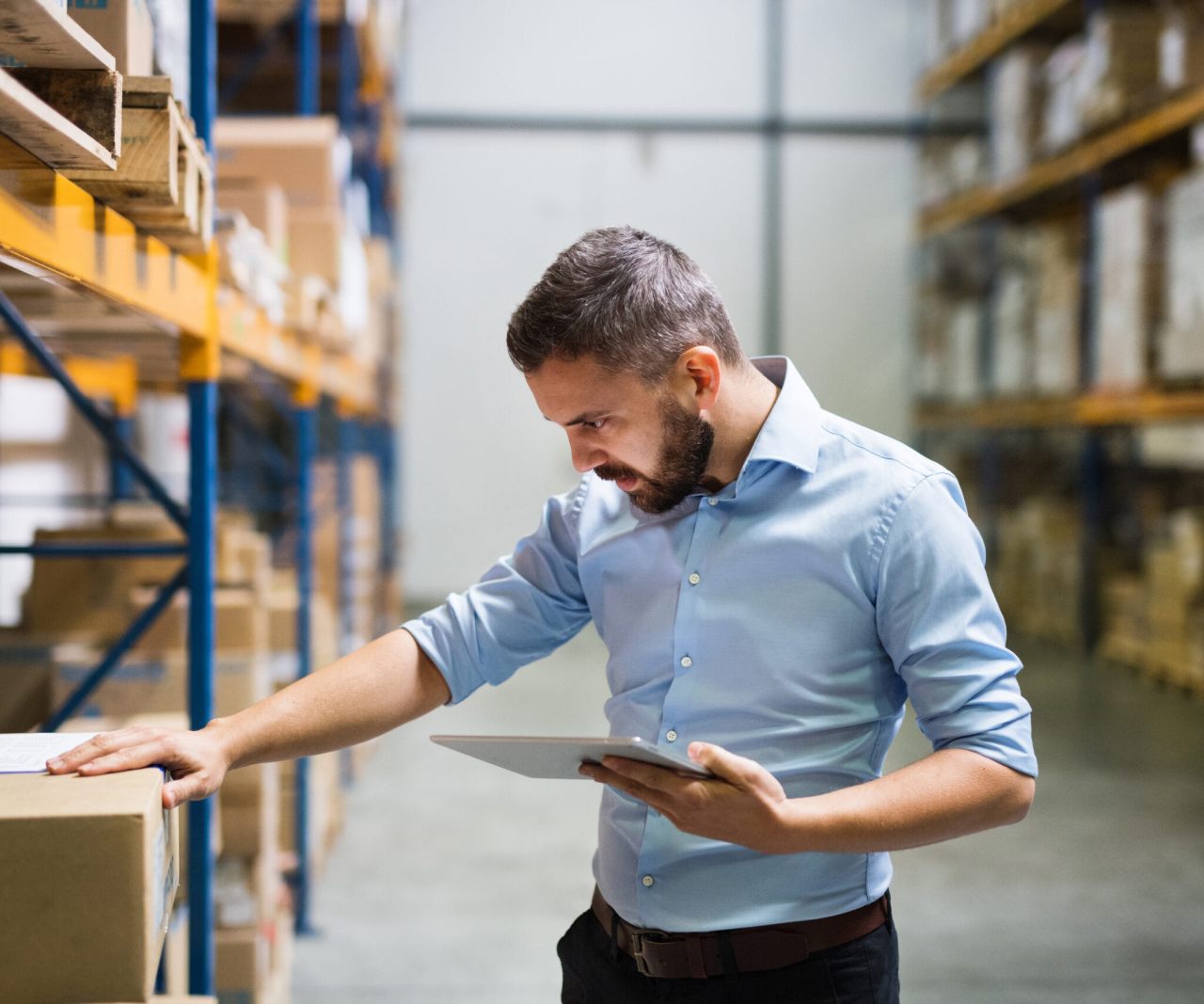 Man holding a tablet in one hand with his other hand on a box, while reading a label on the box