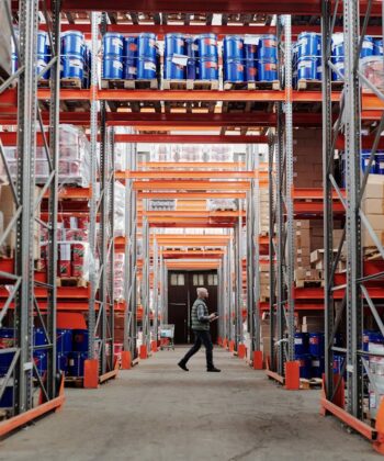 A warehouse worker walking between large shelves of cardboard boxes.