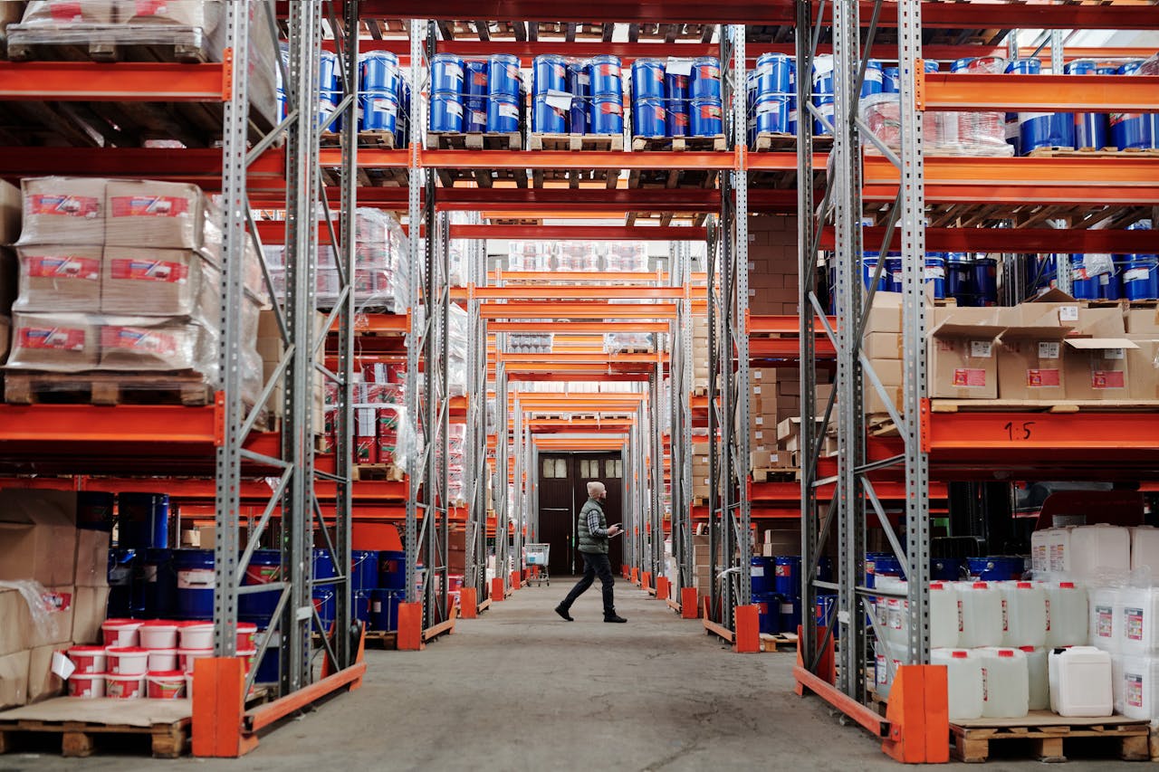 A warehouse worker walking between large shelves of cardboard boxes.