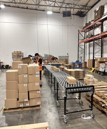 A warehouse worker sorting cardboard boxes, standing next to a conveyor belt.