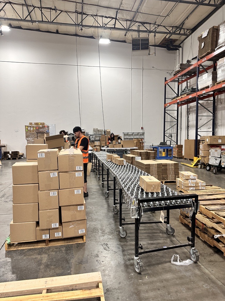 A warehouse worker sorting cardboard boxes, standing next to a conveyor belt.