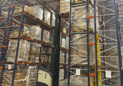 A person operating a lift to take cardboard boxes off of shelves in a warehouse.