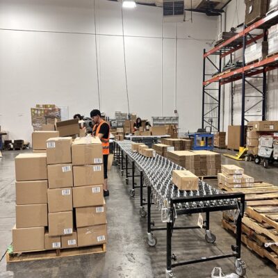 Warehouse workers sorting cardboard boxes, next to a conveyor belt.