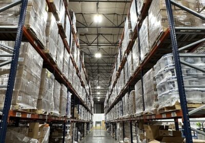 A warehouse aisle, filled with many plastic-wrapped cardboard boxes on shelves.